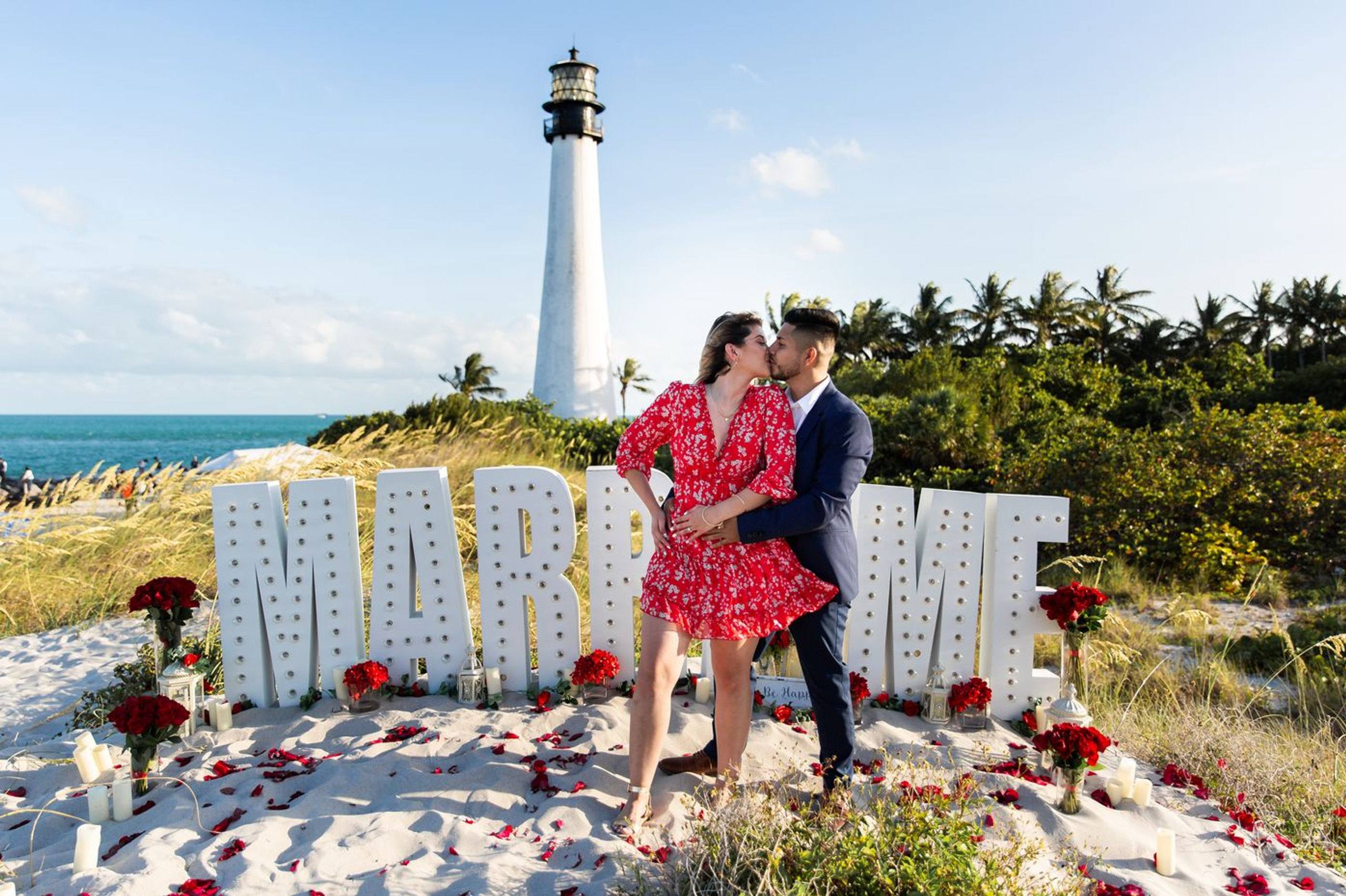 Beach proposal setup with a lighthouse and large letters