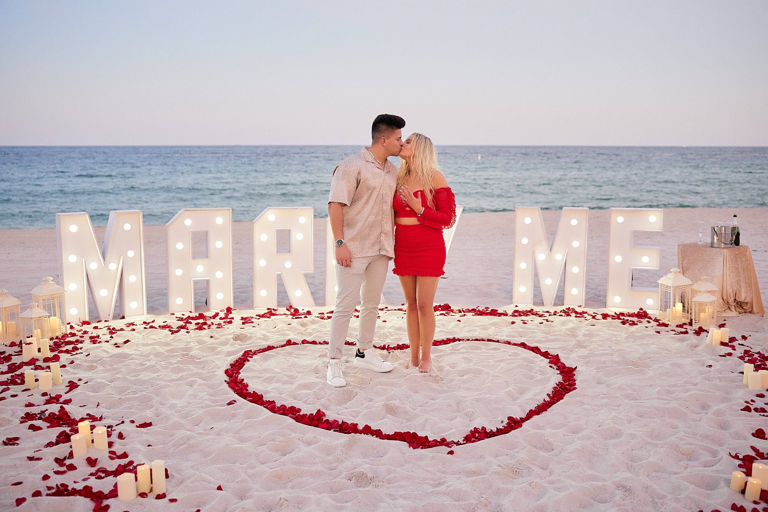Couple in front of illuminated Marry Me letters and red roses