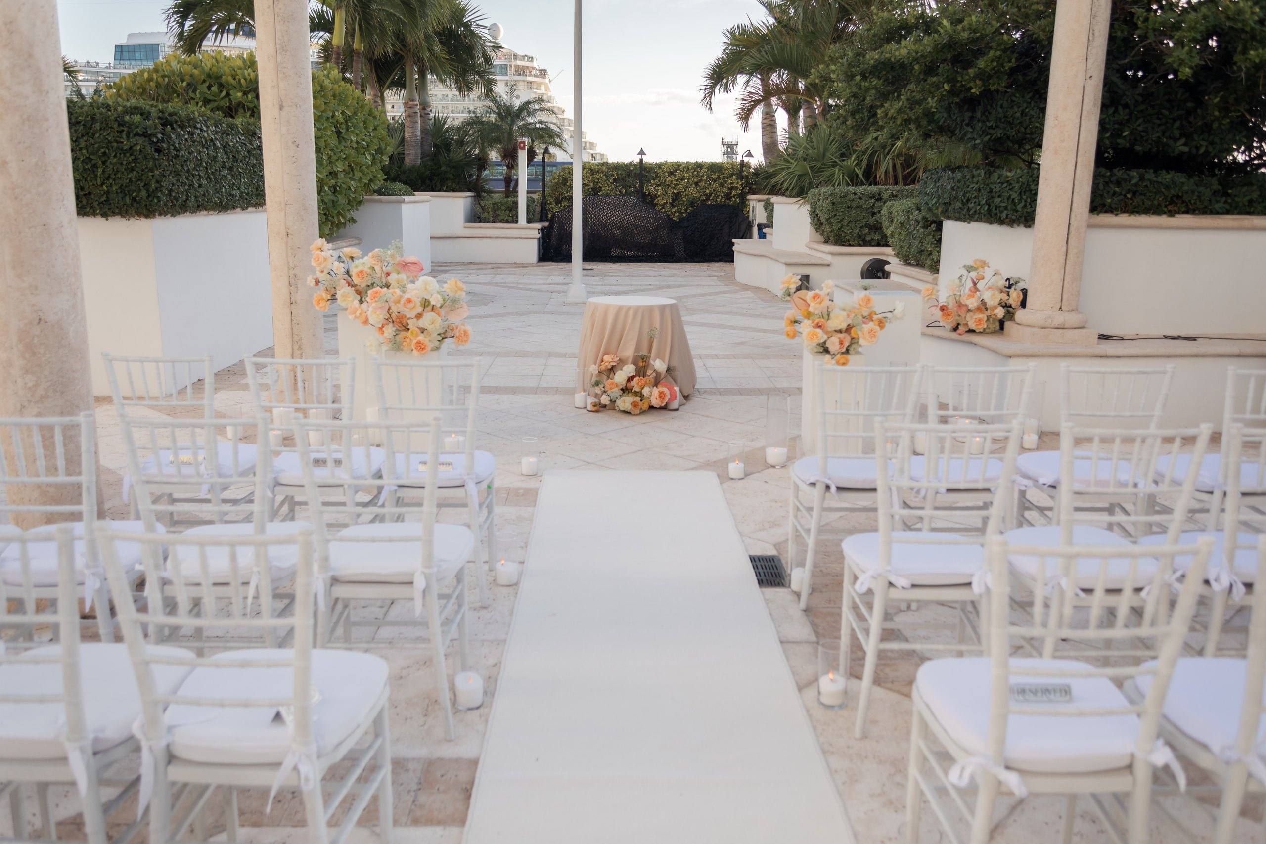 White pedestals with flowers lining an aisle under a pergola