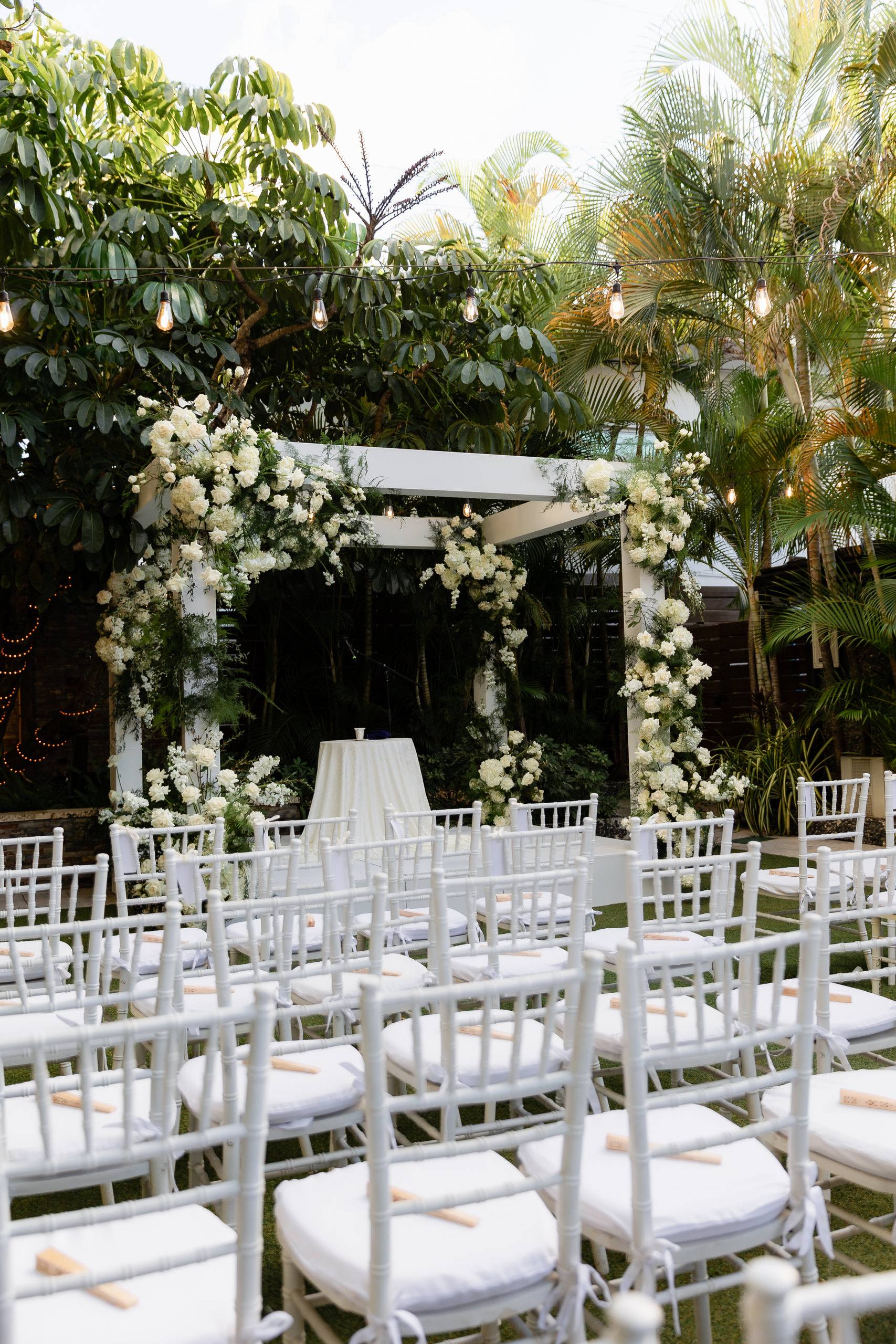 White ceremony chairs beneath a flowered garden canopy